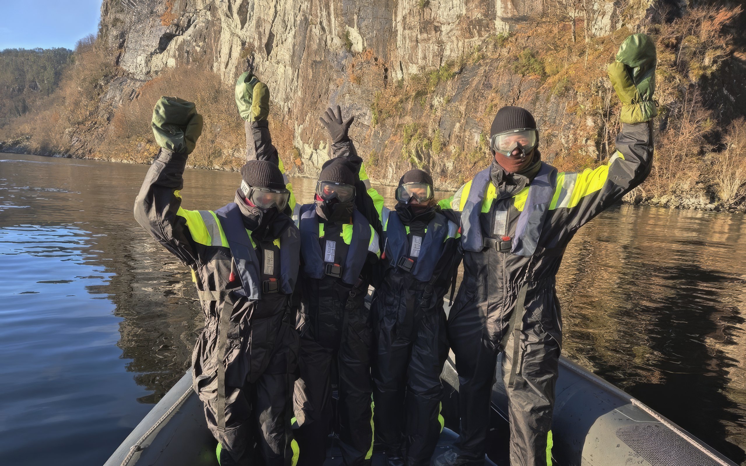 Passengers in safety suits celebrating on a fjord boat with rocky cliffs in the background.