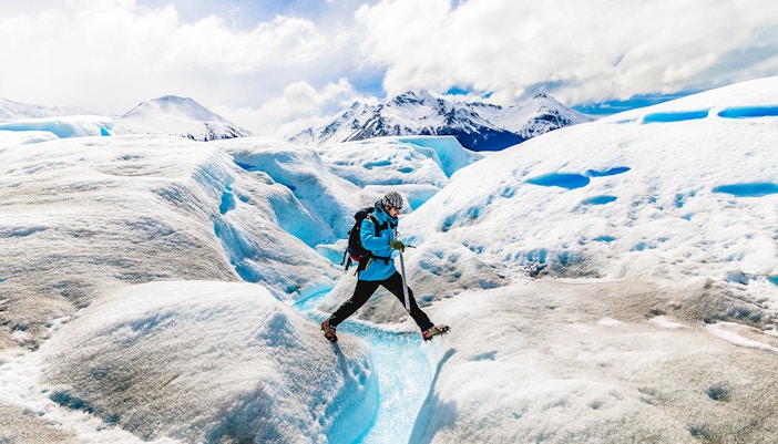 Tourist leaping over ice caves at Big Ice, Perito Moreno Glacier, Argentina.