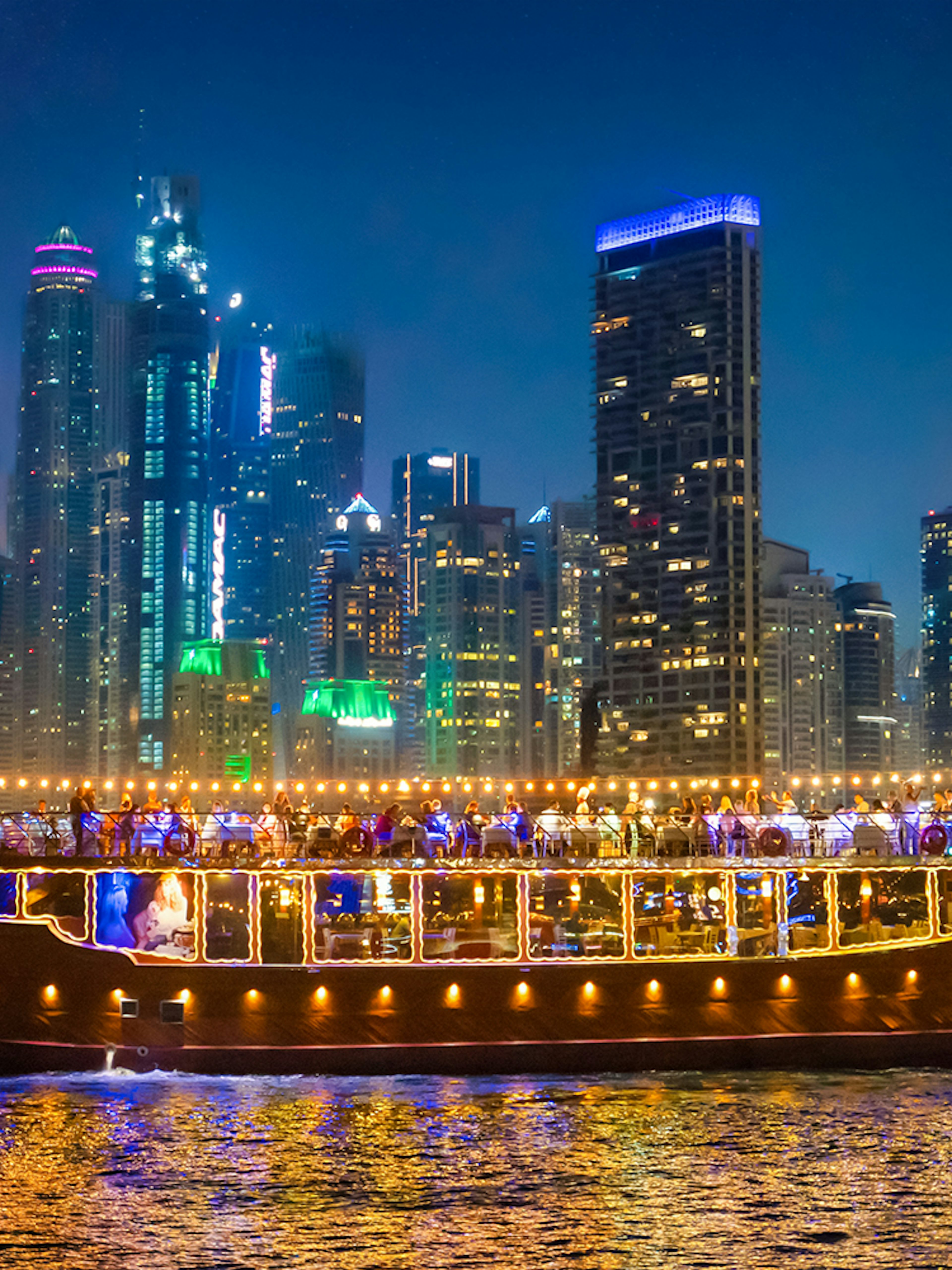 Luxury dhow cruise with lights on Dubai Marina at night, skyscrapers in the background.