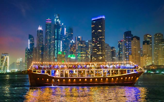 Luxury dhow cruise with lights on Dubai Marina at night, skyscrapers in the background.