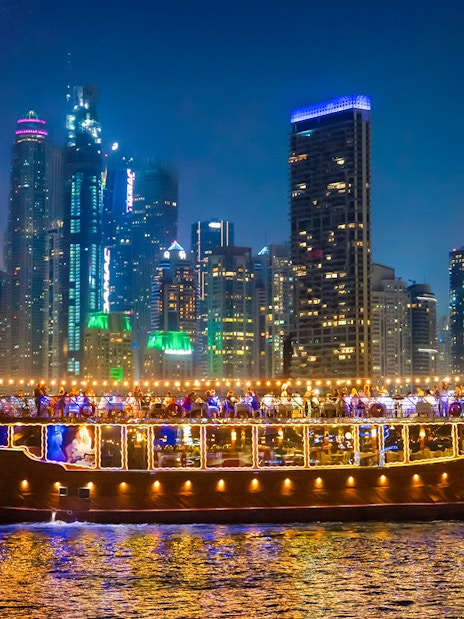Luxury dhow cruise with lights on Dubai Marina at night, skyscrapers in the background.