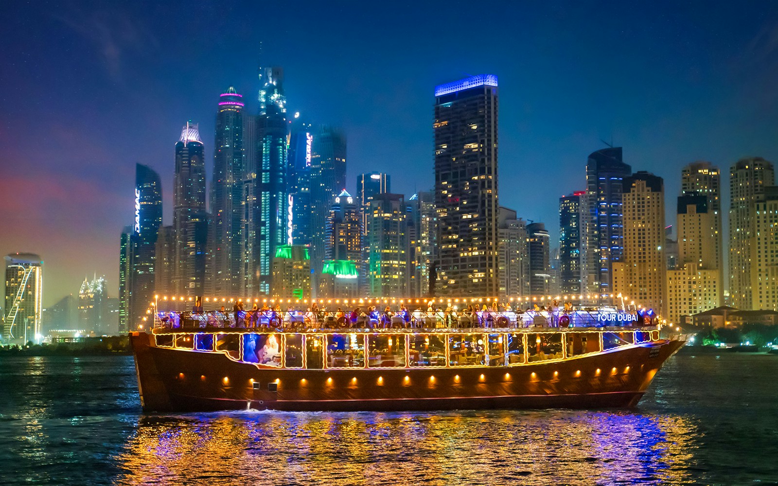 Luxury dhow cruise with lights on Dubai Marina at night, skyscrapers in the background.