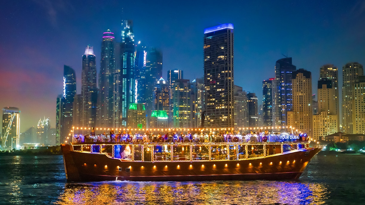 Luxury dhow cruise with lights on Dubai Marina at night, skyscrapers in the background.