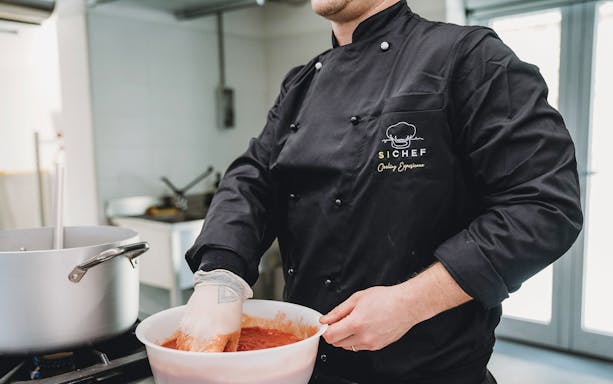 Chef preparing tomato sauce in a cooking class kitchen.