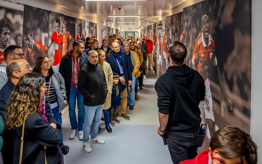 Visitors on a guided tour at Benfica Stadium museum hallway with player murals.