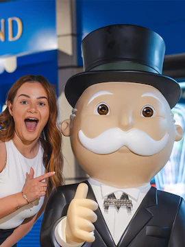 Person posing with Monopoly mascot at Monopoly Dreams attraction.