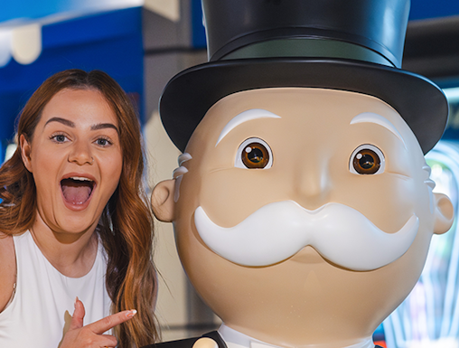 Person posing with Monopoly mascot at Monopoly Dreams attraction.