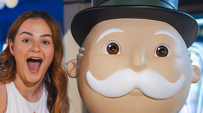 Person posing with Monopoly mascot at Monopoly Dreams attraction.