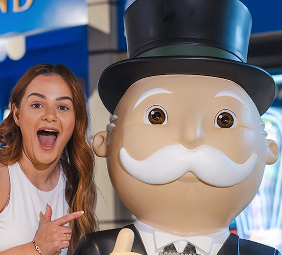 Person posing with Monopoly mascot at Monopoly Dreams attraction.
