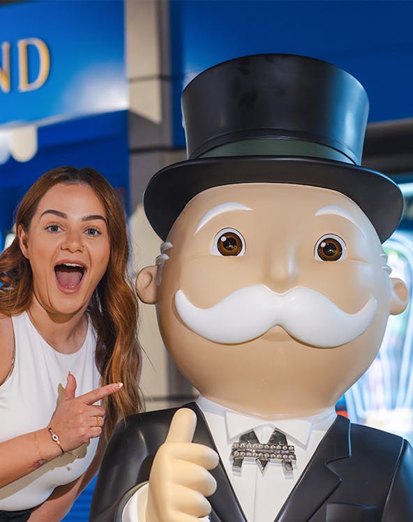 Person posing with Monopoly mascot at Monopoly Dreams attraction.