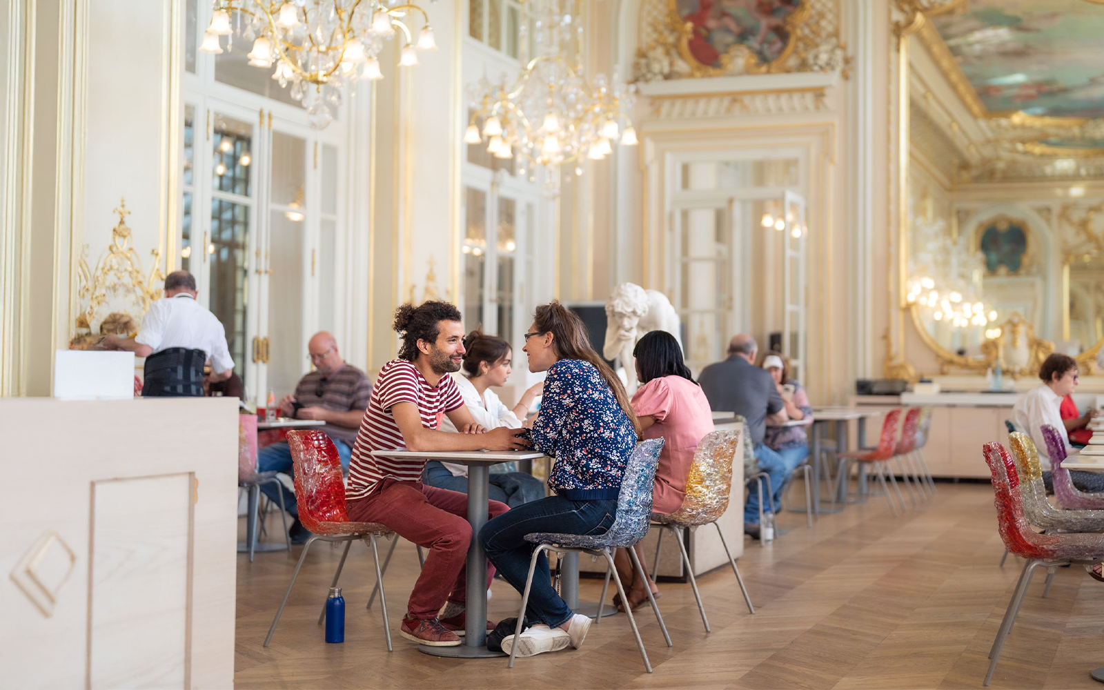 Visitors dining in the ornate café at Musée d’Orsay, Paris, surrounded by chandeliers and art.