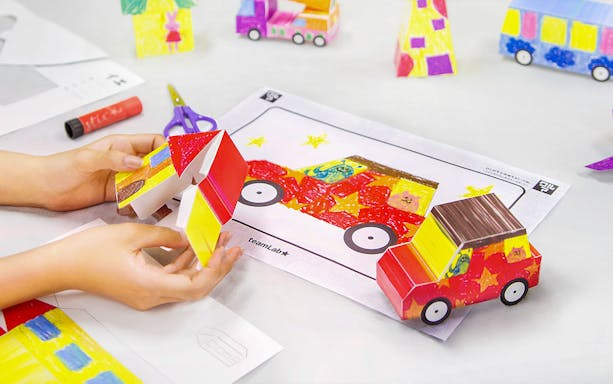 Hands assembling a colorful paper car model at teamLab Future Park.