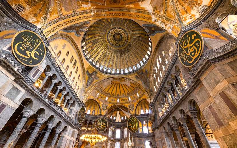 Interior view of Hagia Sophia's dome and arches in Istanbul, showcasing intricate mosaics and calligraphy.