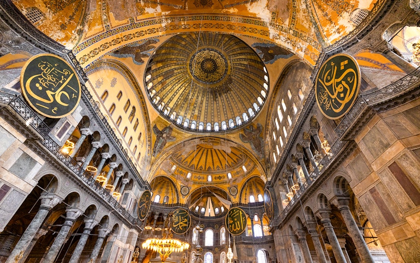 Interior view of Hagia Sophia's dome and arches in Istanbul, showcasing intricate mosaics and calligraphy.