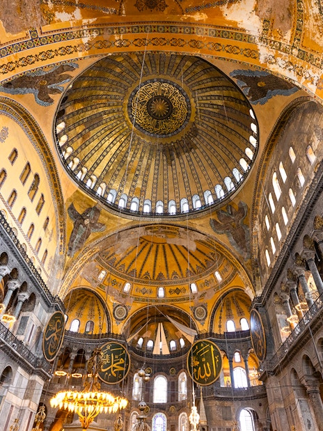 Interior view of Hagia Sophia's dome and arches in Istanbul, showcasing intricate mosaics and calligraphy.