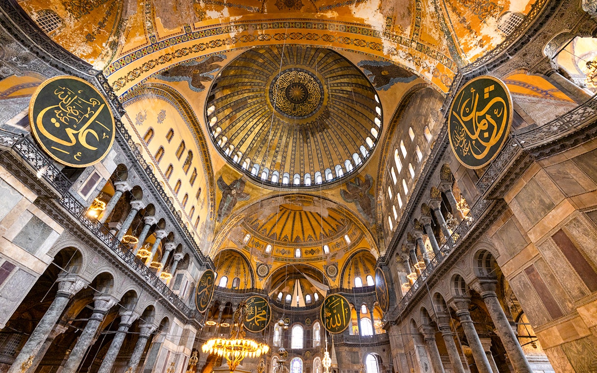 Interior view of Hagia Sophia's dome and arches in Istanbul, showcasing intricate mosaics and calligraphy.