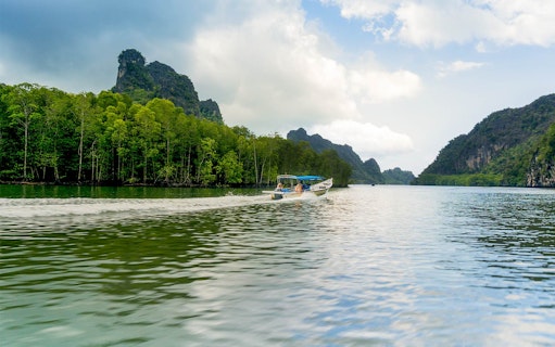 Speedboat cruising along the riverside of Kilim Park with lush greenery and rocky hills.