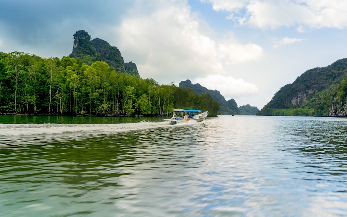 Speedboat cruising along the riverside of Kilim Park with lush greenery and rocky hills.
