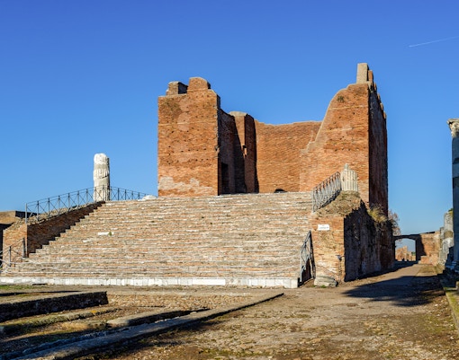 Ancient ruins of Ostia Antica with brick structure and stone columns under clear sky.