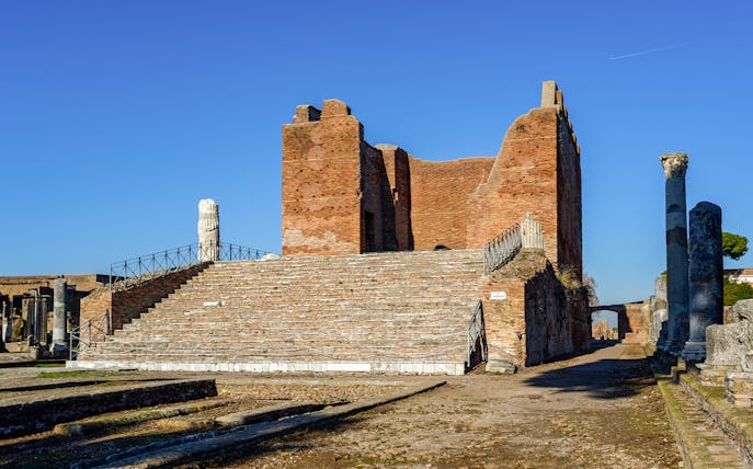Ancient ruins of Ostia Antica with brick structure and stone columns under clear sky.