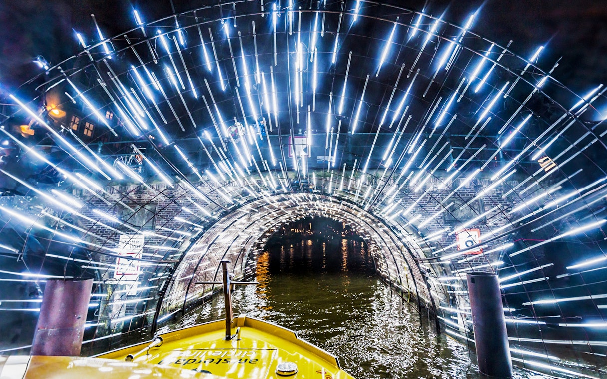 Amsterdam canal cruise passing through illuminated tunnel during Light Festival.