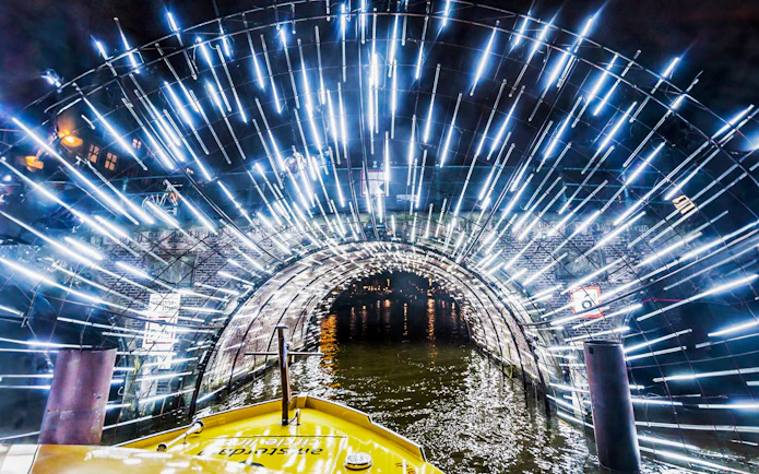 Amsterdam canal cruise passing through illuminated tunnel during Light Festival.