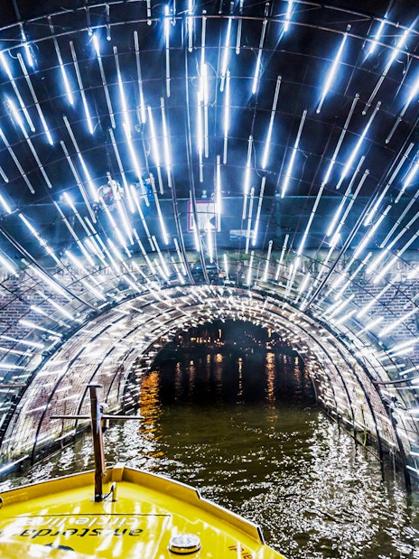 Amsterdam canal cruise passing through illuminated tunnel during Light Festival.