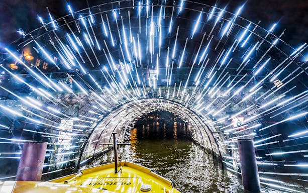 Amsterdam canal cruise passing through illuminated tunnel during Light Festival.