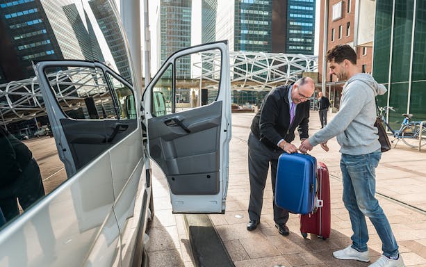 Driver helping passenger with luggage by van at airport.