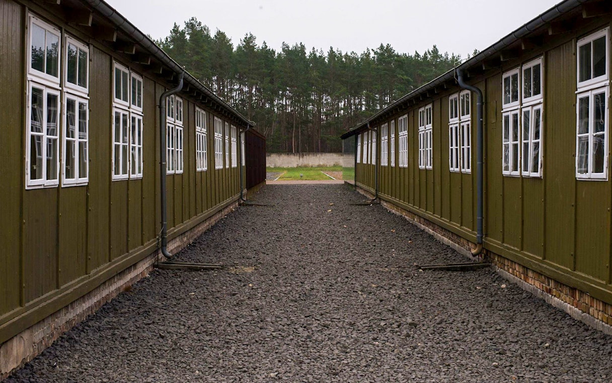 Sachsenhausen Concentration Camp barracks with gravel path and forest background.