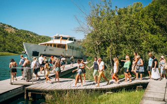 Tourists walking on a wooden path near a boat at Krka National Park.
