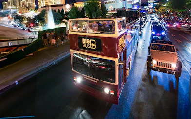 Big Bus night tour on road in Madrid with city lights in background.