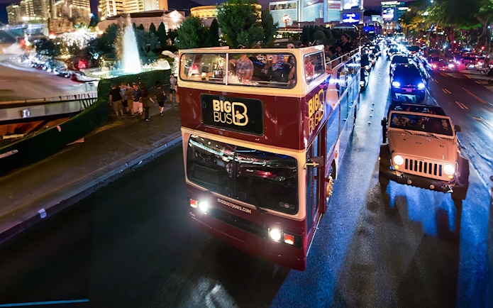 Big Bus night tour on road in Madrid with city lights in background.