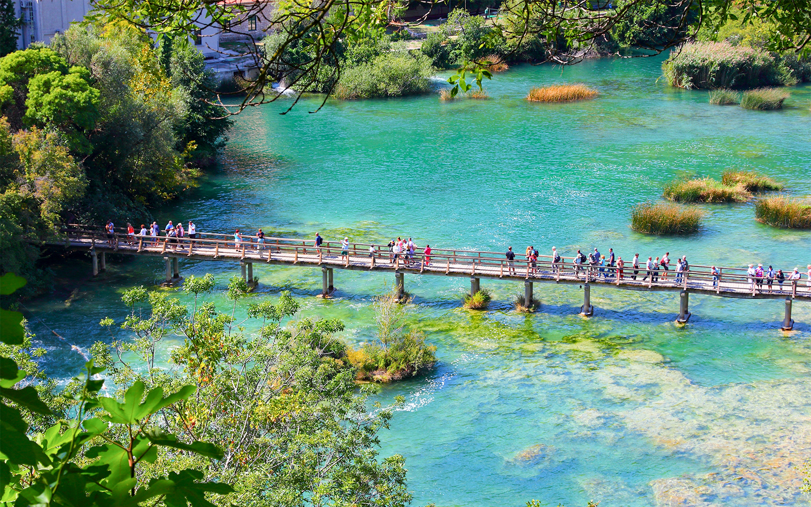 People walking on a wooden bridge over turquoise water in Krka National Park, Croatia.
