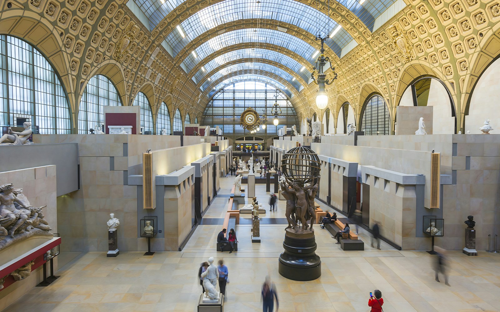 Innenansicht des Musée d'Orsay in Paris mit Skulpturen, Besuchern und der großen Uhr im Hintergrund