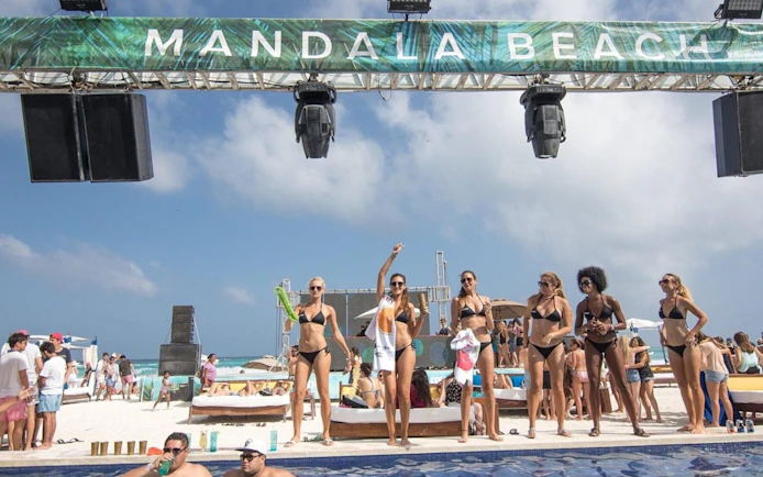 People enjoying a sunny day at Mandala Beachclub Cancun, with a pool and beach in the background.