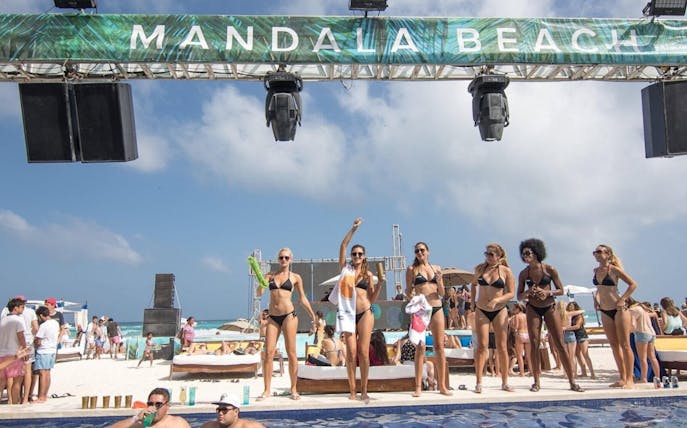 People enjoying a sunny day at Mandala Beachclub Cancun, with a pool and beach in the background.