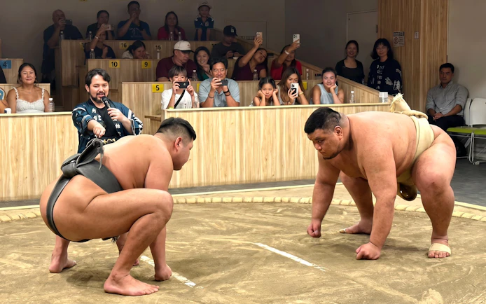 Sumo wrestlers face off in a Kyoto arena during a live show, with an audience watching.