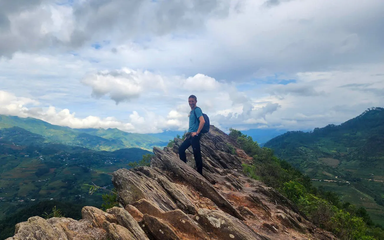 Trekker on rocky ridge with terraced rice fields in Mu Cang Chai, Vietnam.