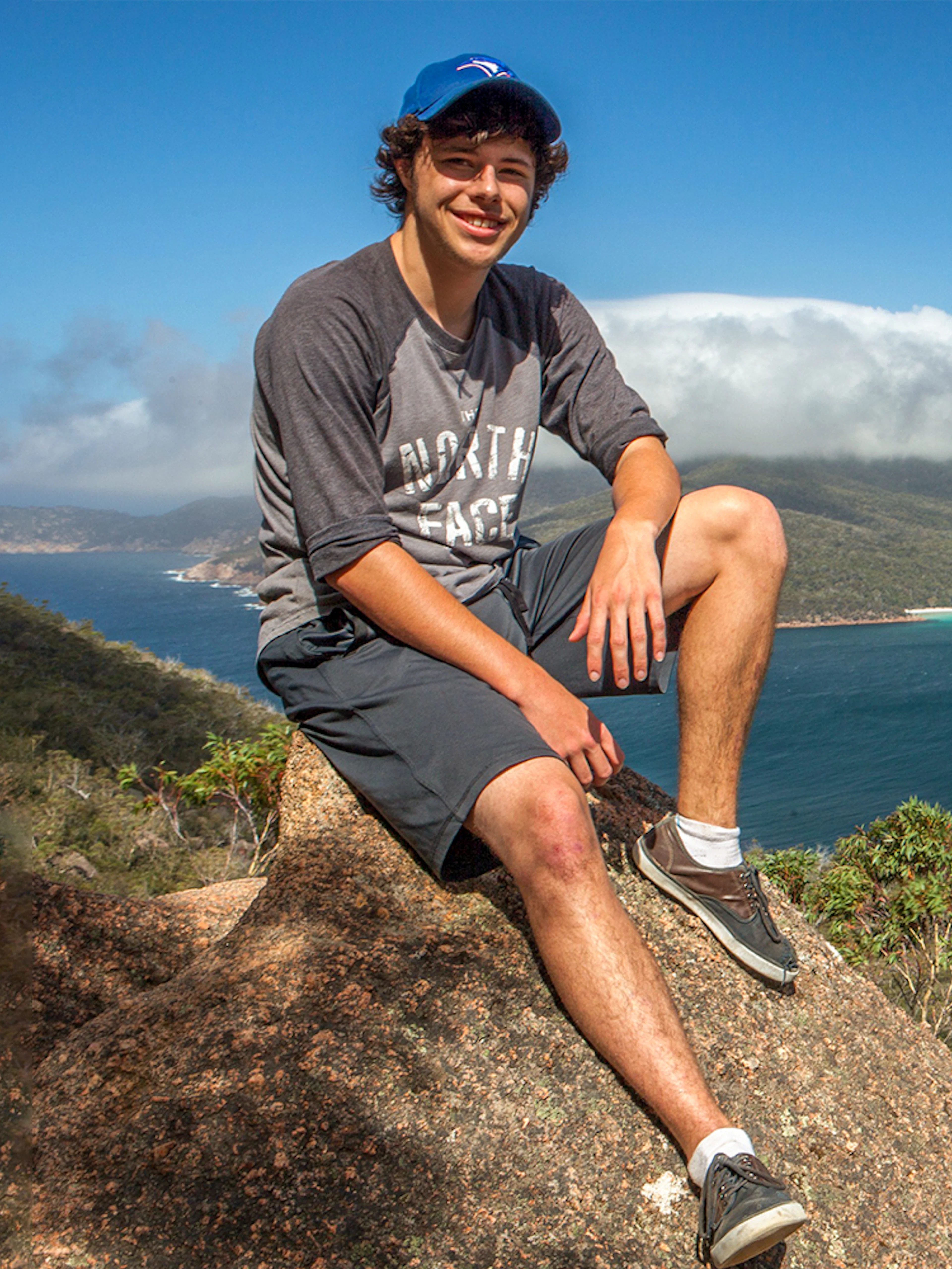 Person sitting on a rock overlooking Wineglass Bay, Tasmania, with lush hills and blue water.
