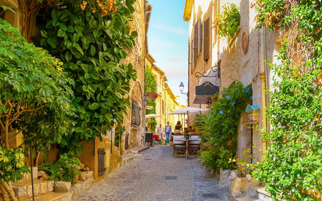 Cobblestone street with cafes and greenery in Saint Paul de Vence, France.