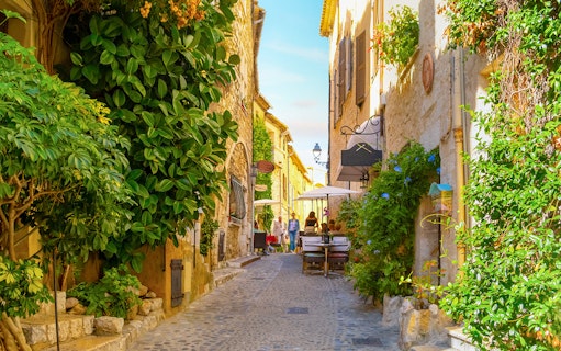 Cobblestone street with cafes and greenery in Saint Paul de Vence, France.