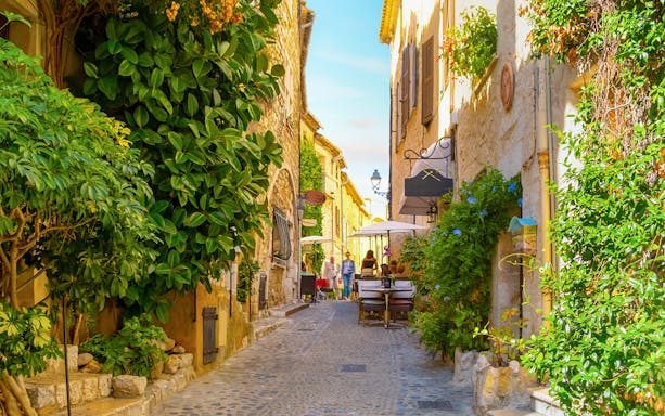 Cobblestone street with cafes and greenery in Saint Paul de Vence, France.