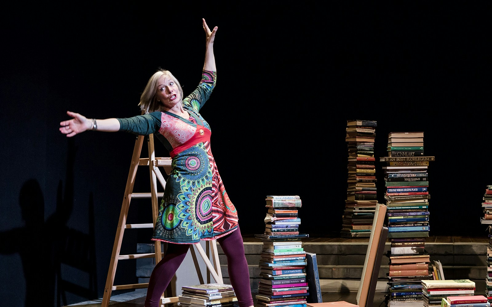 Performer on stage with stacks of books, part of "I Believe In Unicorns" show.