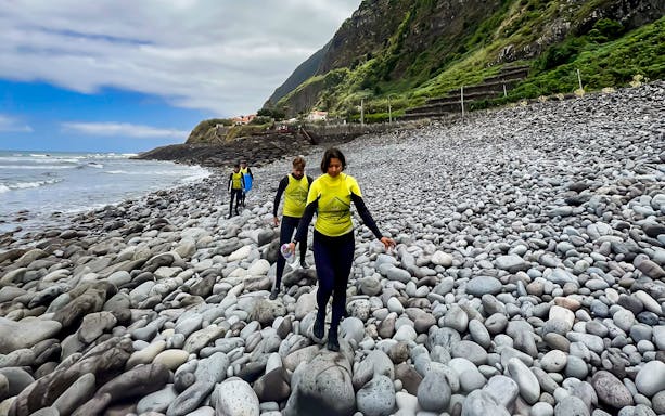 Surfers walking on a rocky beach in Madeira, Portugal, with surfboards and wetsuits.