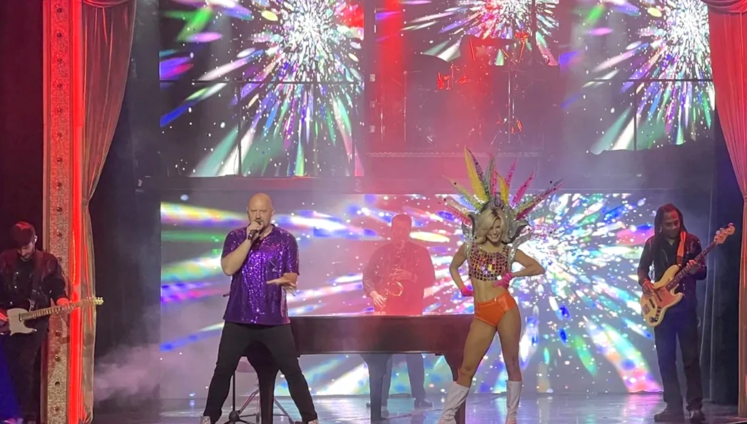 Performer singing on stage with vibrant lights during Piano Man: A Tribute to Elton John & Billy Joel.