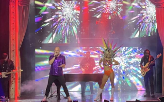 Performer singing on stage with vibrant lights during Piano Man: A Tribute to Elton John & Billy Joel.