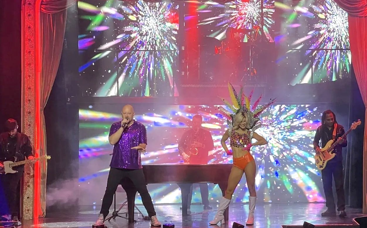 Performer singing on stage with vibrant lights during Piano Man: A Tribute to Elton John & Billy Joel.