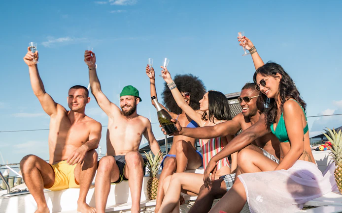Group of friends toasting with champagne on a yacht under a sunny sky.
