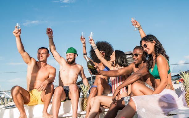 Group of friends toasting with champagne on a yacht under a sunny sky.